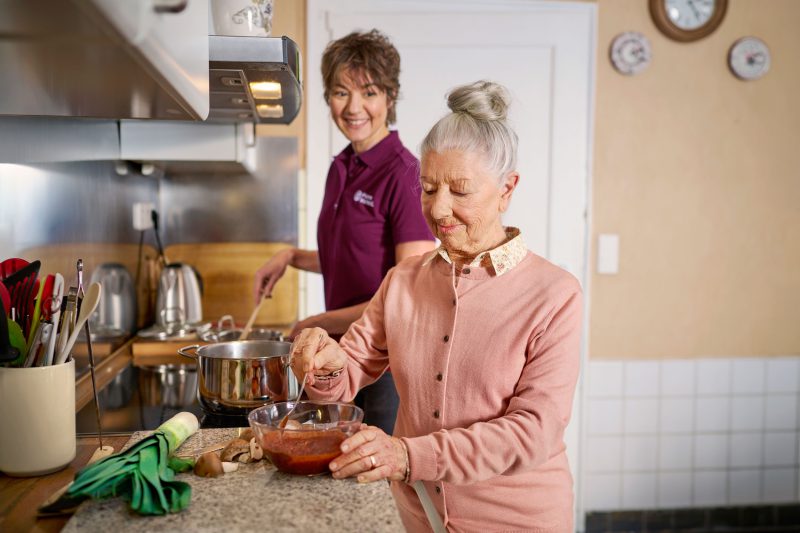 Seniorin mit Betreuungskraft am Herd