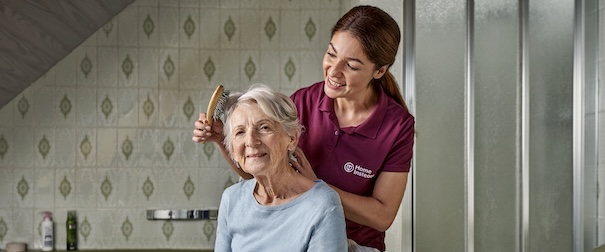 Betreuungskraft kaemmt Seniorin