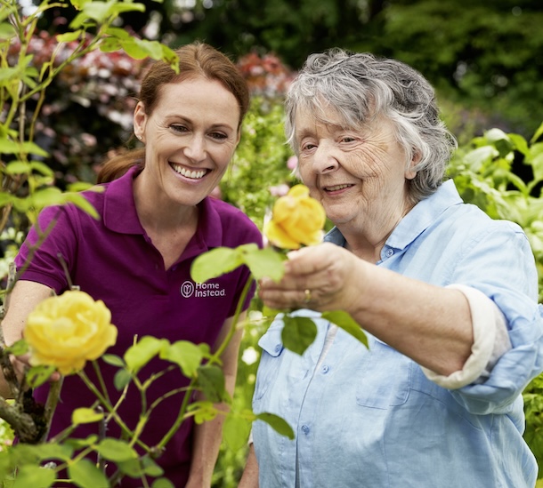 Betreuungskraft ist mit Seniorin im Garten und betrachtet gelbe Rosen