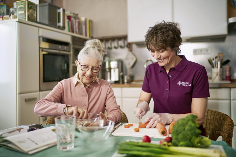 Betreuungskraft kocht gemeinsam mit älterer Dame