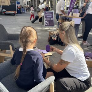 Jenny flechtet eine lila Strähne in die Haare eines Mädchens